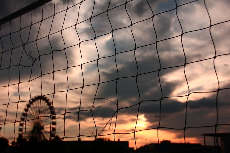 A ferris wheel with an sunset and a tennis net in the foreground
